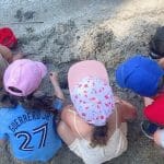 Six young children playing closely together in a sandbox, demonstrating the collaborative nature and science of small class sizes during outdoor learning.